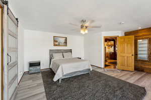 Bedroom with a barn door, baseboards, a ceiling fan, ensuite bath, and wood finished floors