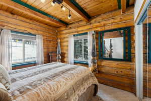 Bedroom with rail lighting, wood ceiling, log walls, and beam ceiling