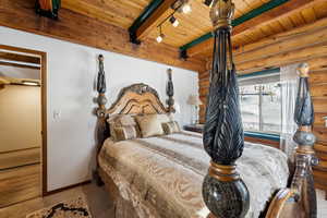 Bedroom with rustic walls, rail lighting, and wooden ceiling