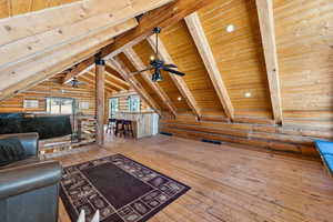 Unfurnished living room with lofted ceiling with beams, ceiling fan, hardwood / wood-style flooring, wood ceiling, and log walls