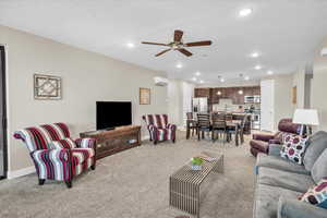 Living area with light carpet, a wall unit AC, baseboards, and recessed lighting