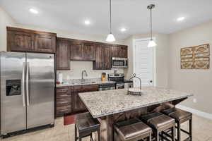 Kitchen with appliances with stainless steel finishes, a kitchen breakfast bar, light stone countertops, a kitchen island with sink, and a sink