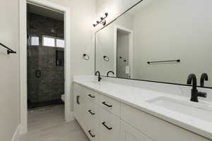 Bathroom featuring double vanity, a sink, toilet, and a shower stall