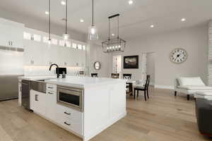 Kitchen featuring built in appliances, a kitchen island with sink, white cabinetry, light countertops, and glass insert cabinets