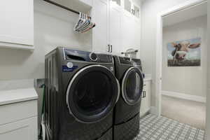 Clothes washing area with baseboards, cabinet space, and washer and dryer