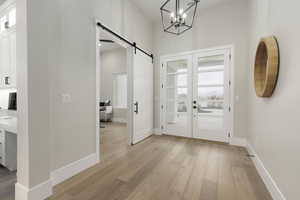 Foyer featuring baseboards, french doors, a barn door, and light wood-style floors