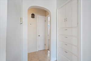 Hallway featuring arched walkways, light tile patterned floors, and baseboards