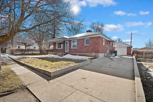 Single story home with brick siding, an outdoor structure, a detached garage, concrete driveway, and a chimney