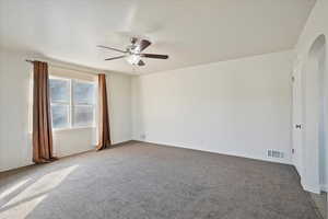 Carpeted spare room with ceiling fan, visible vents, arched walkways, and baseboards