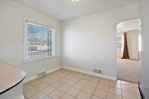 Unfurnished room featuring arched walkways, light tile patterned floors, visible vents, and baseboards