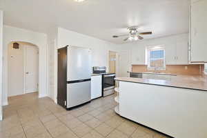 Kitchen with arched walkways, white cabinets, light countertops, appliances with stainless steel finishes, and open shelves