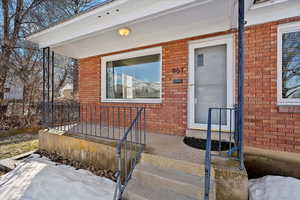 Snow covered property entrance featuring a porch and brick siding