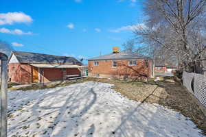 Snow covered property with brick siding and fence