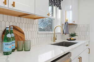 Kitchen featuring plenty of natural light, light stone counters, a sink, white cabinetry, and backsplash