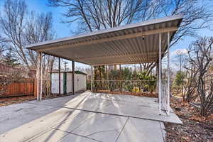 View of patio / terrace featuring a storage shed, an outdoor structure, fence, driveway, and a detached carport