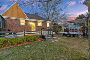 Back of house at dusk featuring a deck, brick siding, a yard, and a chimney