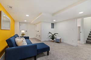 Living area with recessed lighting, light colored carpet, visible vents, baseboards, and stairs