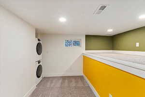 Washroom featuring stacked washer / drying machine, light colored carpet, visible vents, laundry area, and baseboards