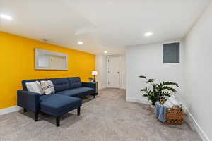 Living area with electric panel, baseboards, visible vents, carpet flooring, and recessed lighting