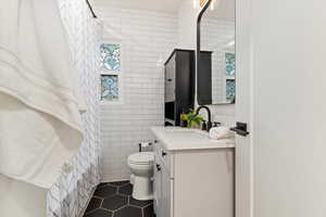 Full bathroom with vanity, tile walls, toilet, and tile patterned floors