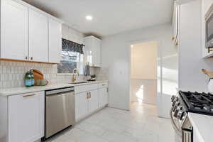 Kitchen featuring stainless steel appliances, marble finish floor, white cabinetry, and backsplash