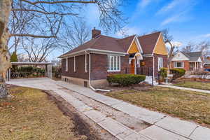 View of front of home with driveway, a front yard, a chimney, and brick siding