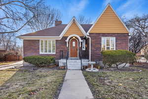 View of front of house featuring brick siding, a chimney, a shingled roof, and a front lawn