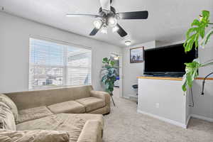 Living room with a textured ceiling, light colored carpet, a ceiling fan, baseboards, and visible vents