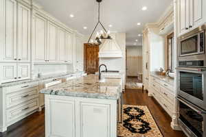 Kitchen featuring appliances with stainless steel finishes, a center island with sink, hanging light fixtures, and dark wood-style floors