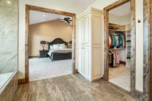 Bedroom with light wood-style floors, light carpet, vaulted ceiling, and a spacious closet