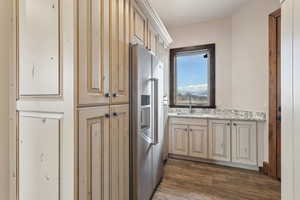 Kitchen with cream cabinets, dark wood-style flooring, a sink, high end fridge, and light stone countertops