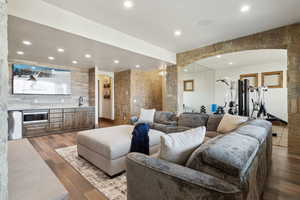 Living area with arched walkways, indoor wet bar, wood finished floors, and recessed lighting