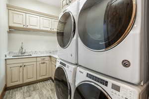 Laundry room featuring stacked washer / drying machine, cabinet space, light wood-style flooring, a sink, and independent washer and dryer