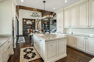 Kitchen with light stone counters, decorative light fixtures, dark wood finished floors, a sink, and an island with sink