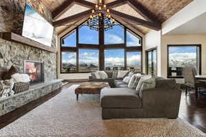 Living area with wooden ceiling, dark wood-type flooring, an inviting chandelier, a stone fireplace, and high vaulted ceiling