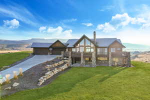 View of front of house with a chimney, concrete driveway, a mountain view, stone siding, and a front lawn