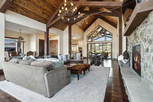 Living area with dark wood-style floors, a notable chandelier, wood ceiling, a stone fireplace, and high vaulted ceiling