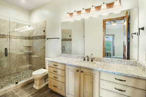 Bathroom featuring toilet, a stall shower, wood finished floors, and vanity