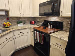 Kitchen with dark wood-style flooring, decorative backsplash, light brown cabinetry, light stone countertops, and black appliances