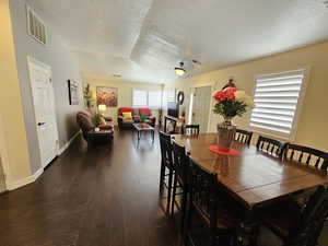 Dining space with a textured ceiling, dark wood-type flooring, visible vents, and baseboards