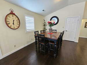 Dining space with dark wood-type flooring, visible vents, vaulted ceiling, and baseboards