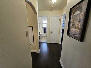 Hallway with baseboards, arched walkways, a textured wall, dark wood-style flooring, and a textured ceiling