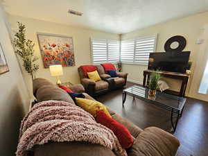 Living room with dark wood-type flooring, visible vents, and baseboards