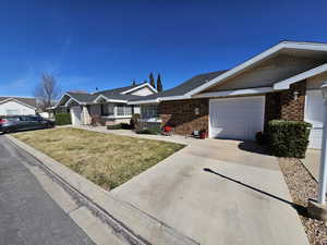 Single story home featuring concrete driveway, brick siding, an attached garage, and a front yard