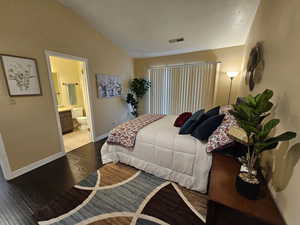 Bedroom with lofted ceiling, visible vents, ensuite bathroom, wood finished floors, and baseboards