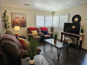 Living room with dark wood-style floors, a textured ceiling, visible vents, and baseboards