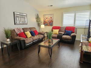 Living area with baseboards, visible vents, dark wood-type flooring, vaulted ceiling, and a textured ceiling