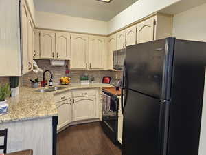 Kitchen featuring tasteful backsplash, dark wood-style flooring, light stone countertops, black appliances, and a sink