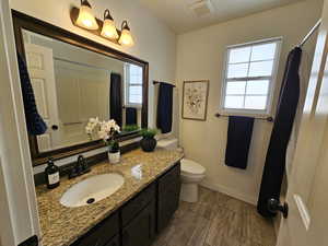 Bathroom featuring wood finish floors, visible vents, toilet, vanity, and baseboards