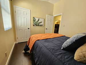 Bedroom featuring lofted ceiling, dark wood-style floors, baseboards, and arched walkways